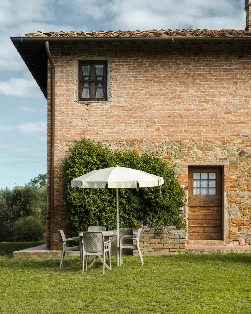 Facciata in mattoni di un agriturismo toscano con ombrellone e tavolo in giardino