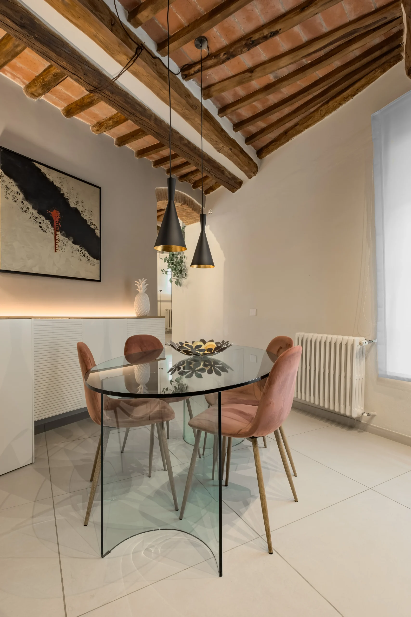 Sala da pranzo con tavolo in vetro, sedie rosa e soffitto con travi in legno